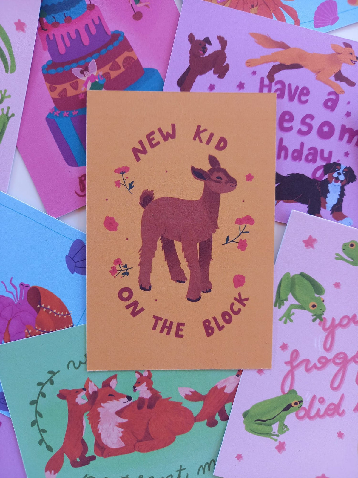 a collection of greeting cards showing animals and fairies on colourful background, the main focus is on a yellow greeting card featuring a baby goat and the text 'new kid on the block'